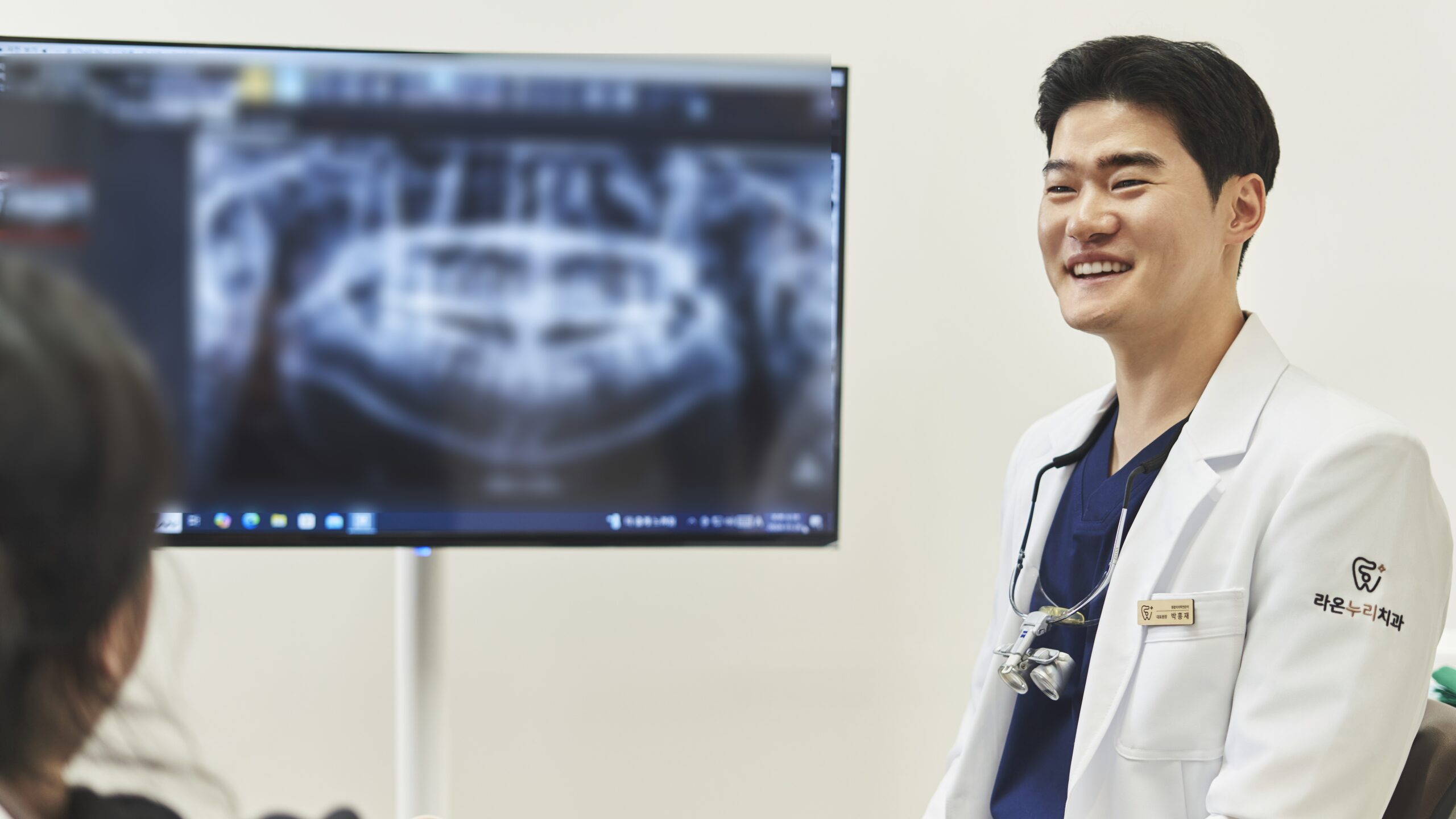 치과 의사가 환자와 상담하며 모니터에 띄워진 엑스레이 영상을 설명하는 모습으로, 치과 의사의 환자 상담 및 정밀 진단 과정을 나타냅니다.